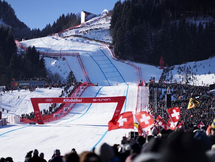 A skier shortly before crossing the finish line in Kitzbühel. An Audi logo and the words Kitzbühel and e-tron can be seen on the red finish arch.