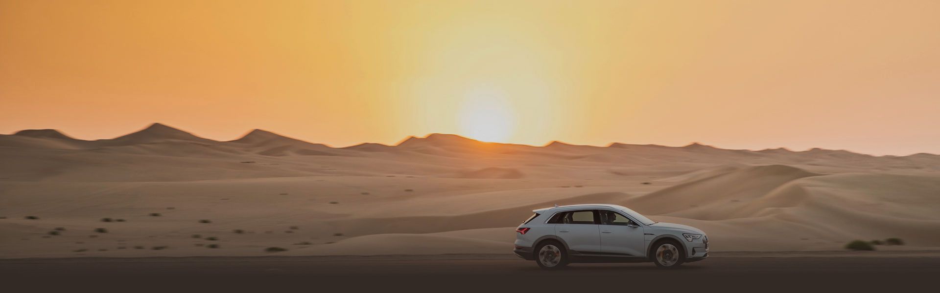 Audi fährt in einer Wüste bei Sonnenuntergang