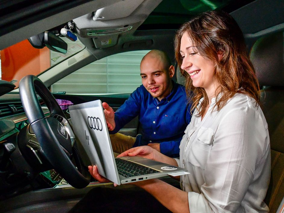 Two graduates sitting in a car with laptop