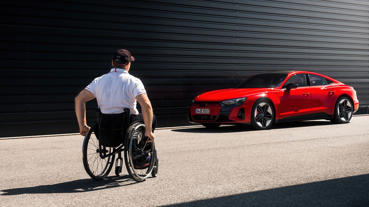 Mann im Rollstuhl nähert sich einem roten Audi e-tron GT