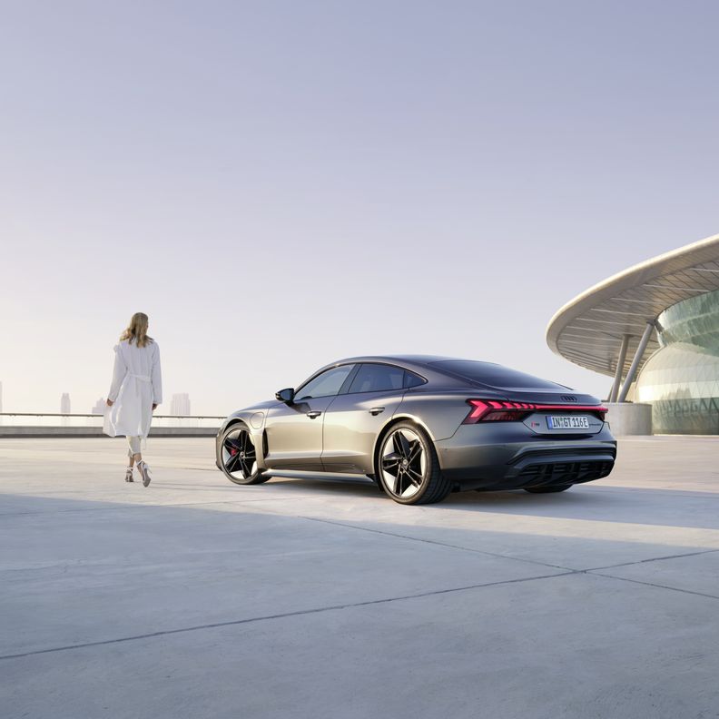 Frau geht neben einem Audi RS e-tron GT vor futuristischer Kulisse