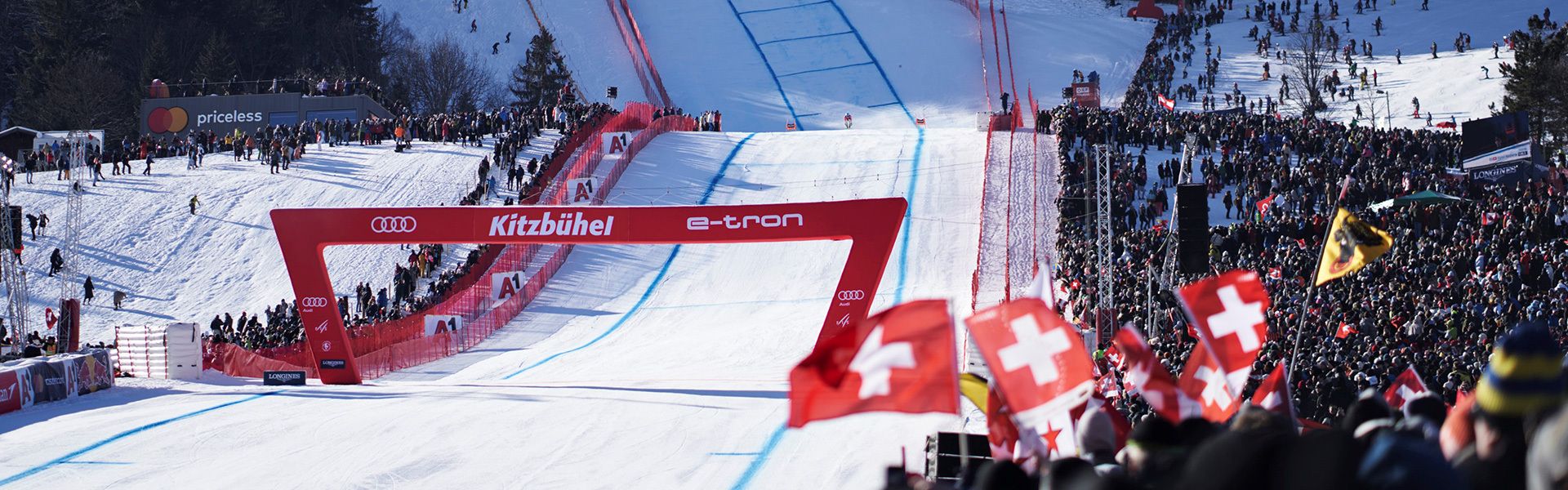 A skier shortly before crossing the finish line in Kitzbühel. An Audi logo and the words Kitzbühel and e-tron can be seen on the red finish arch.