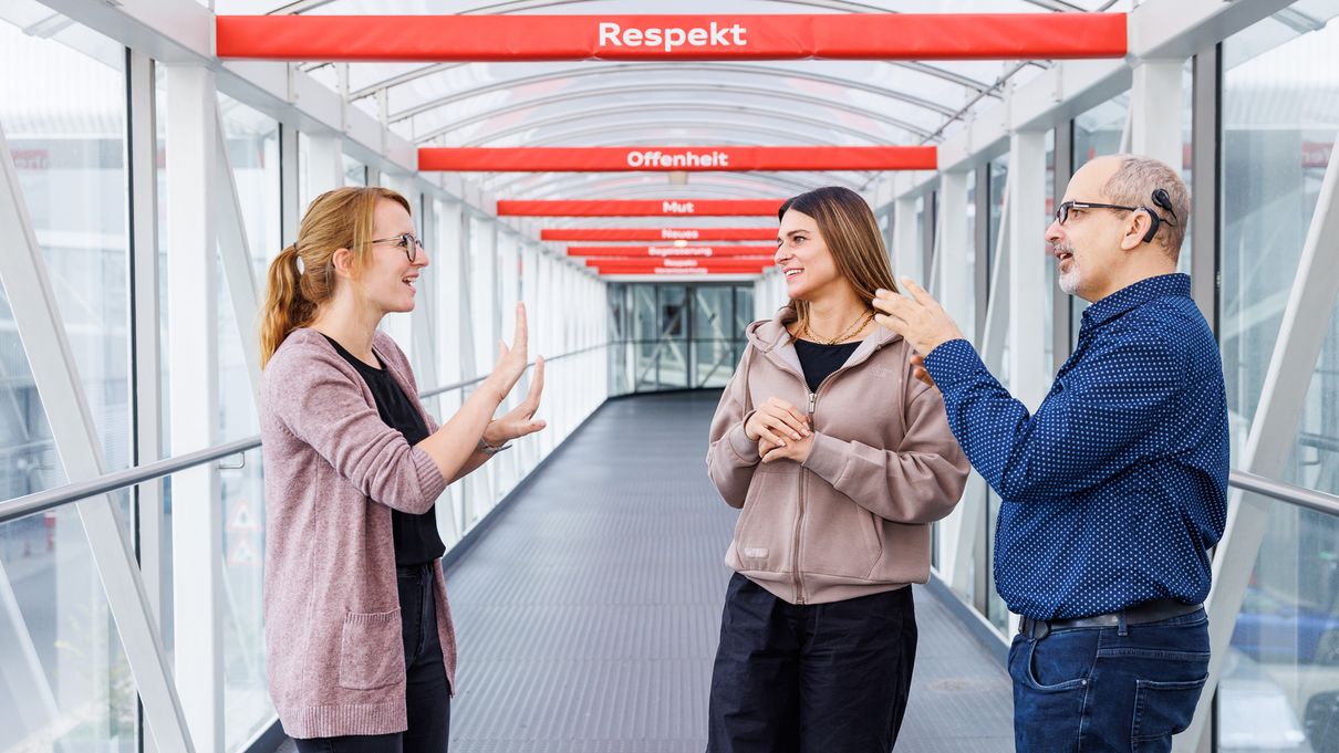 Audian Vanessa with sign language interpreter Vanessa Stöhrl and her colleague Mathias standing in a hallway.