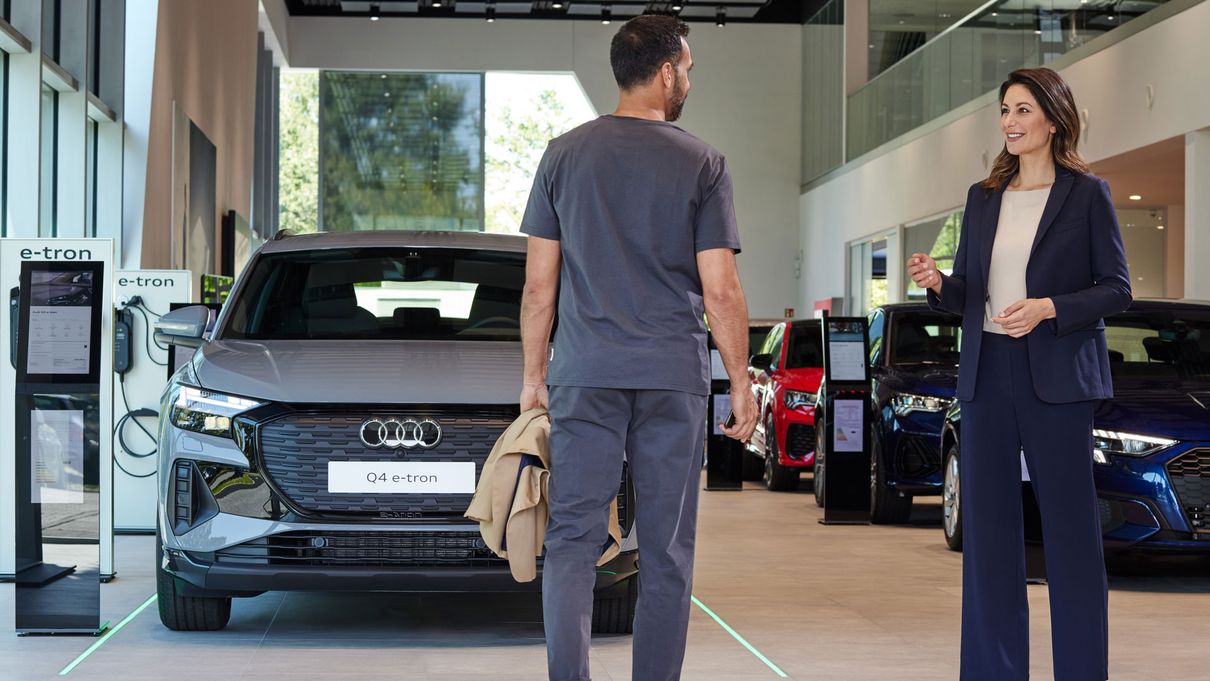 a woman and a man in an Audi dealership stand in front of several vehicles