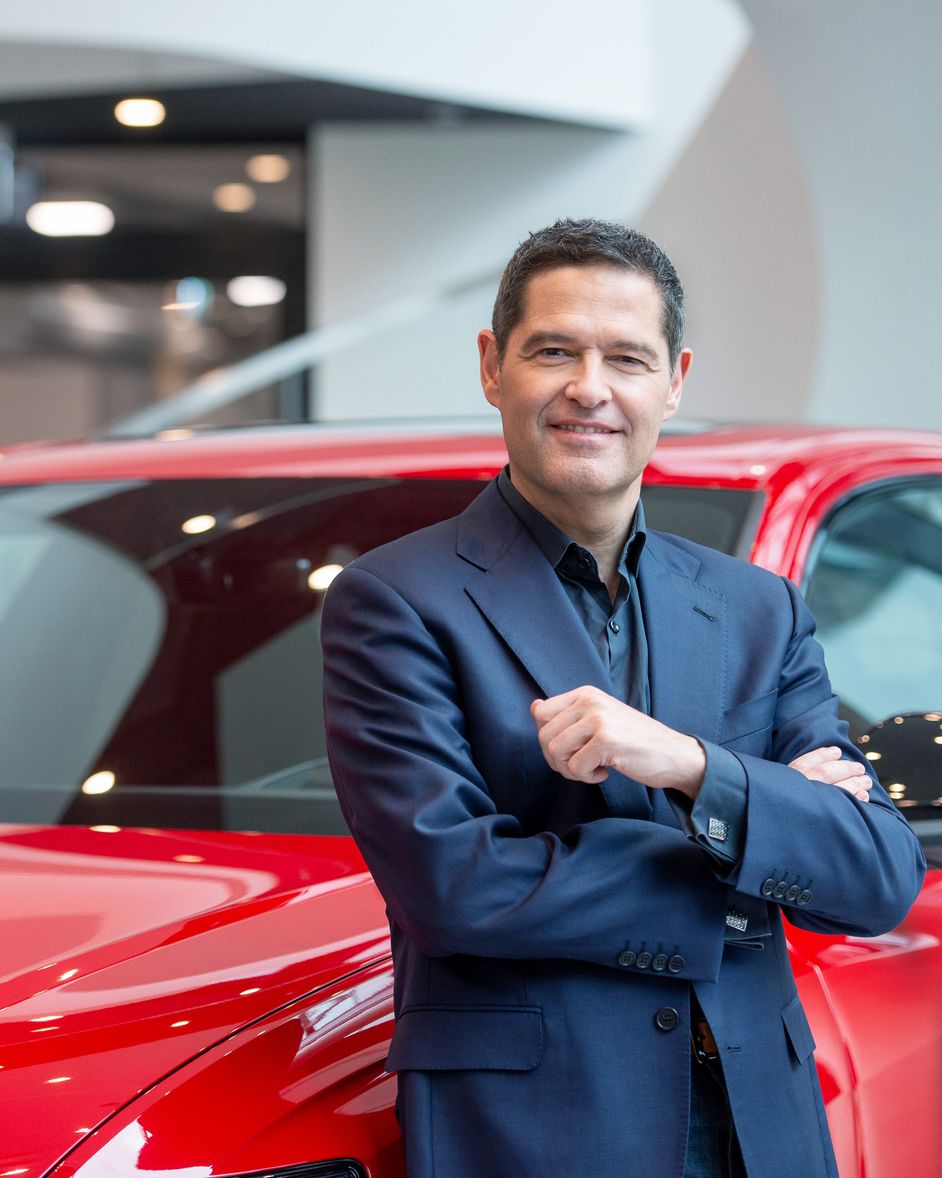 Xavier Ros is standing in front of a red car and is smiling