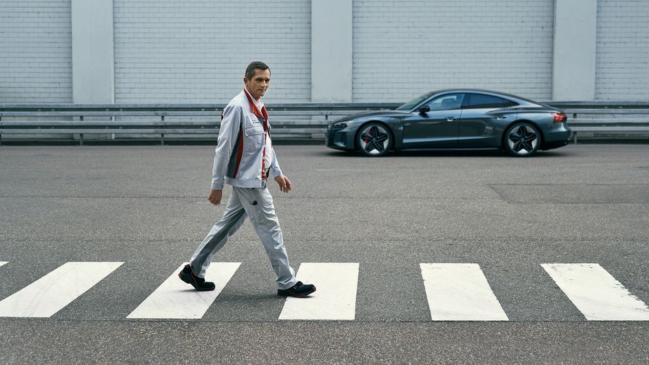 Heinrich Kampa geht auf einer Straße mit einem Audi im Hintergrund
