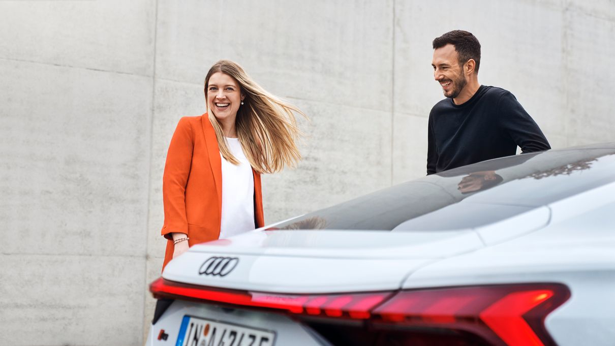 Two people standing behind car and laughing