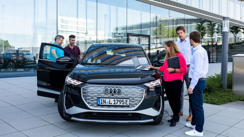 Fünf Menschen stehen an offenen Fahrzeugtüren eines Audi und unterhalten sich