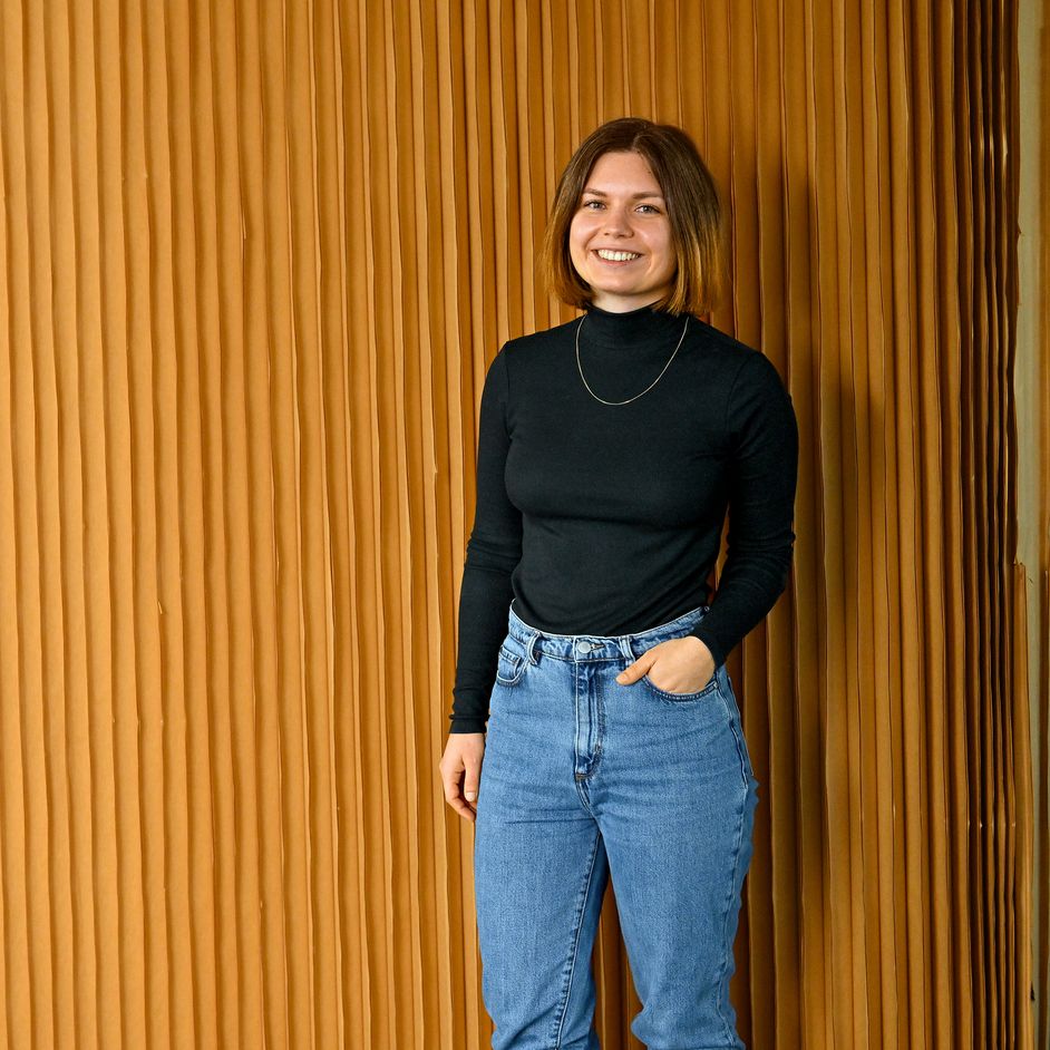 Lisa, Product Designer SDC, stands in front of a wooden wall and laughs into the camera