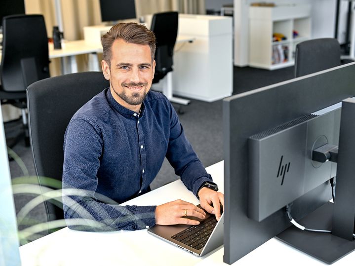 Markus, Product Manager SCD, sits at his laptop and laughs into the camera