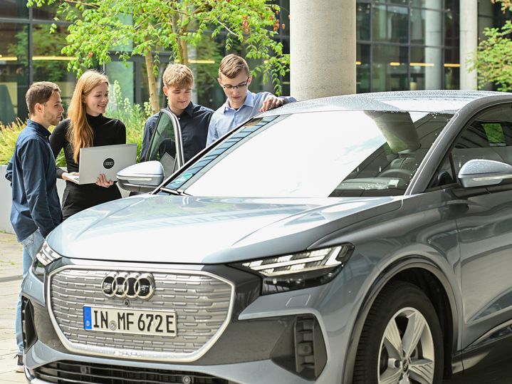 Four Audi employees are in conversation and stand behind an Audi