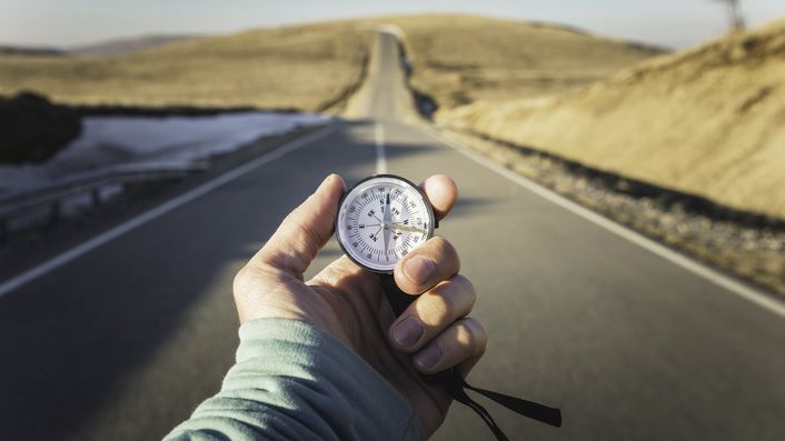 hand holding compass in front of a road