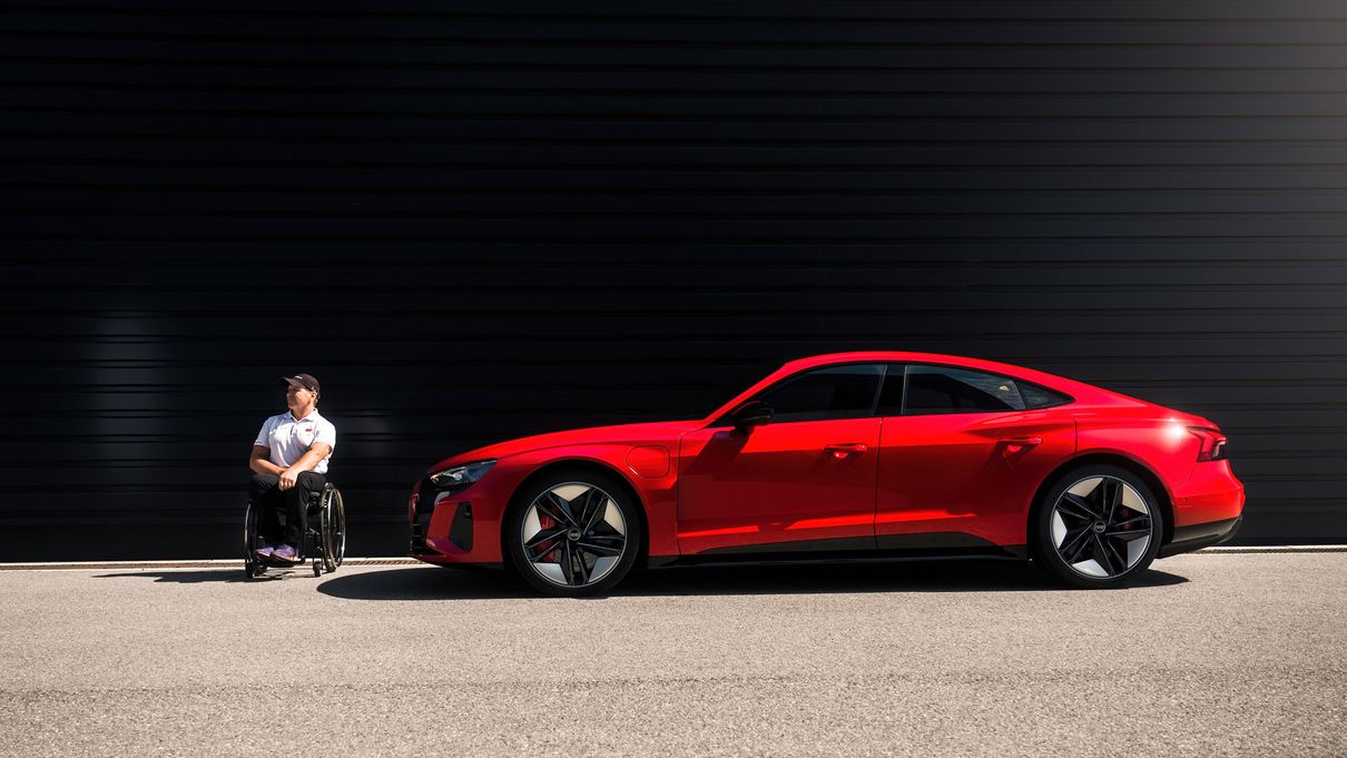 Mann im Rollstuhl neben einem roten Audi e-tron GT
