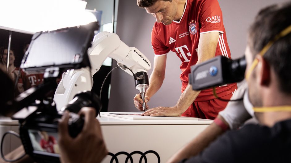 Thomas Müller gibt ein Autogramm mit einem Stift an einem Roboterarm