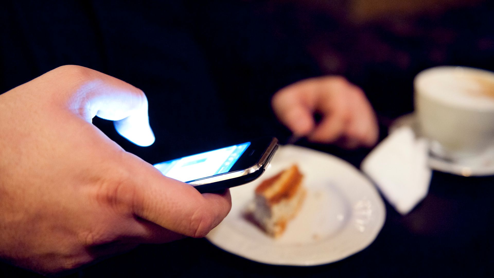 A hand with a cell phone in front of a cake plate