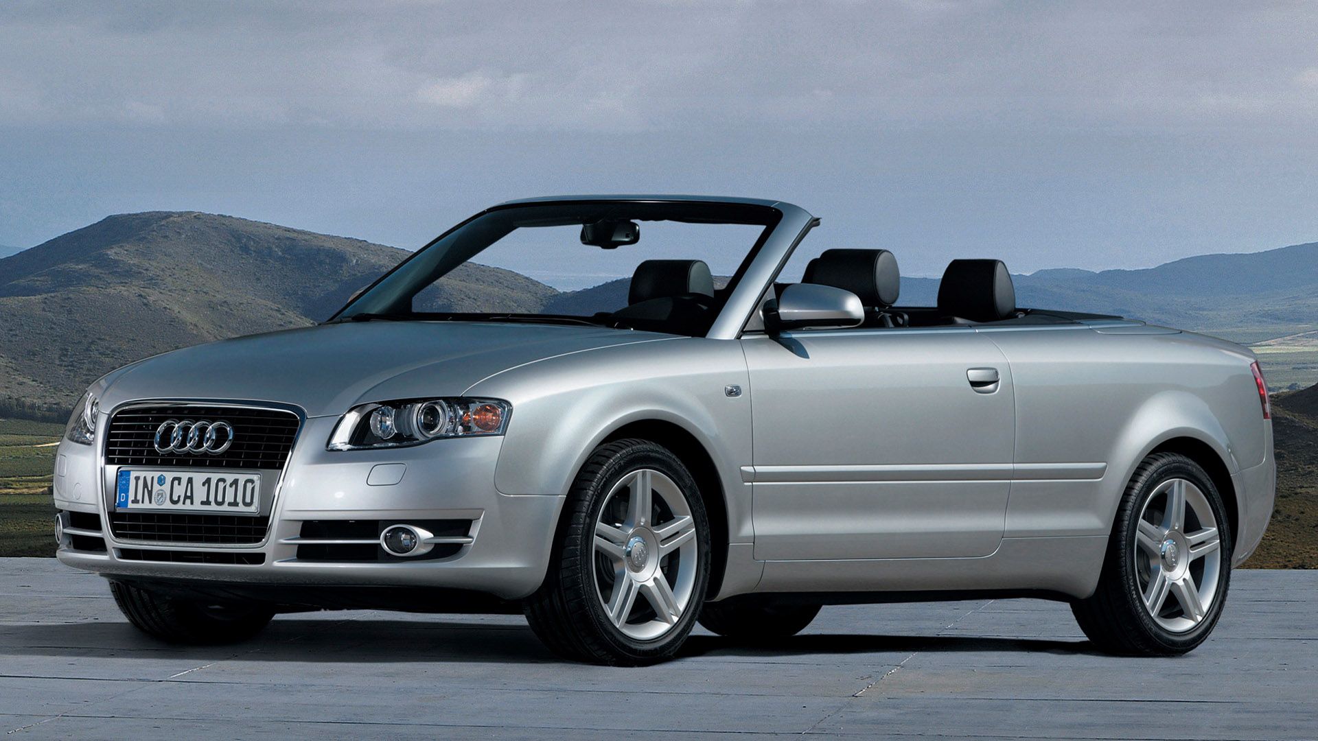 Silver Audi A4 convertible with open top, in the background a valley landscape and mountains