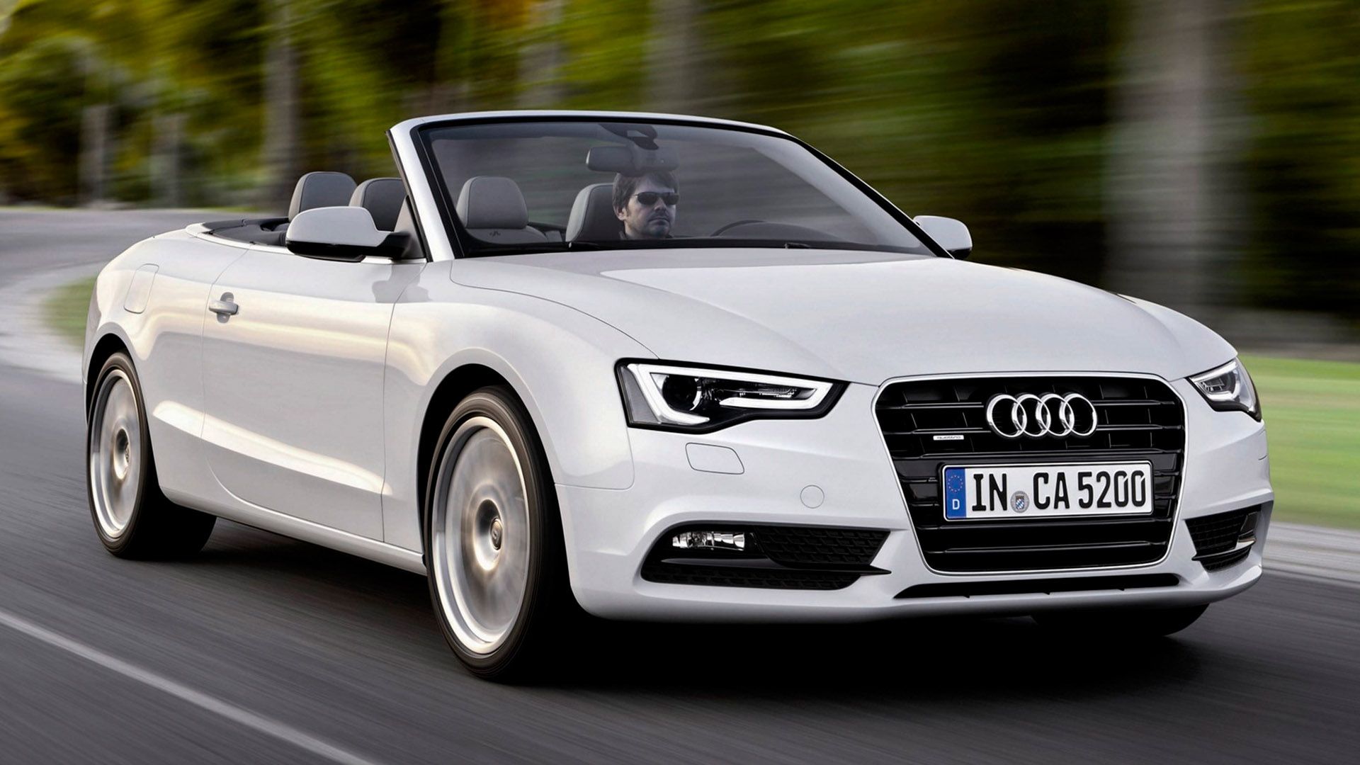 A man with sunglasses sits in an open-top Audi A5 convertible and drives along a country road
