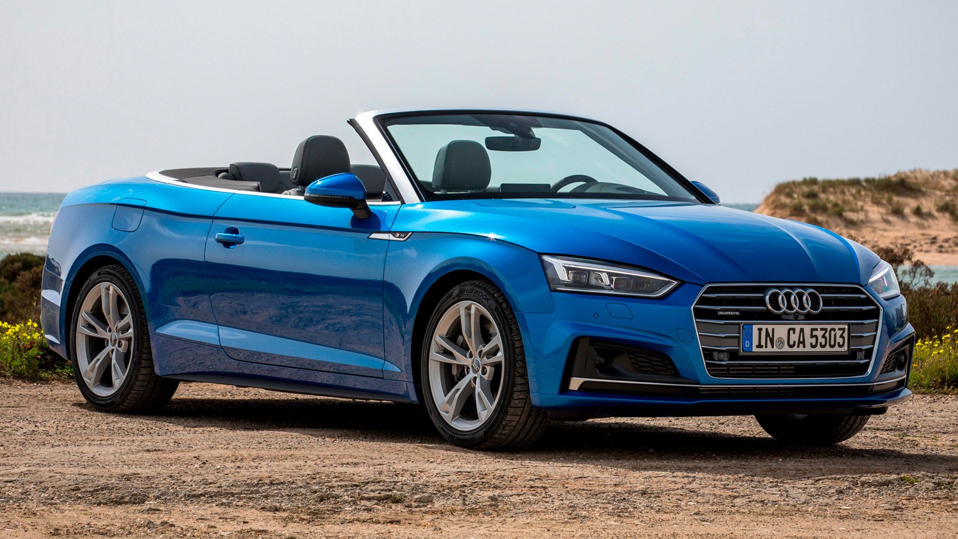 Blue Audi A5 convertible with open top stands on a cliff by the sea on sandy ground