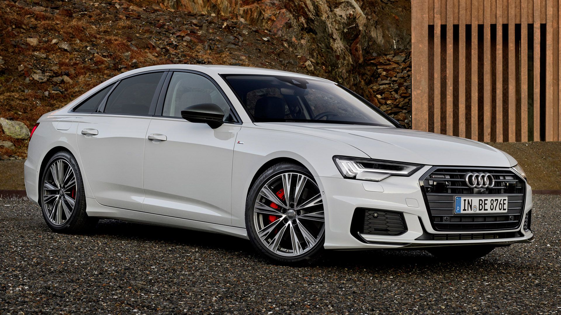White Audi TFSIe with red brake discs standing in a courtyard, a mountain with leaves in the background