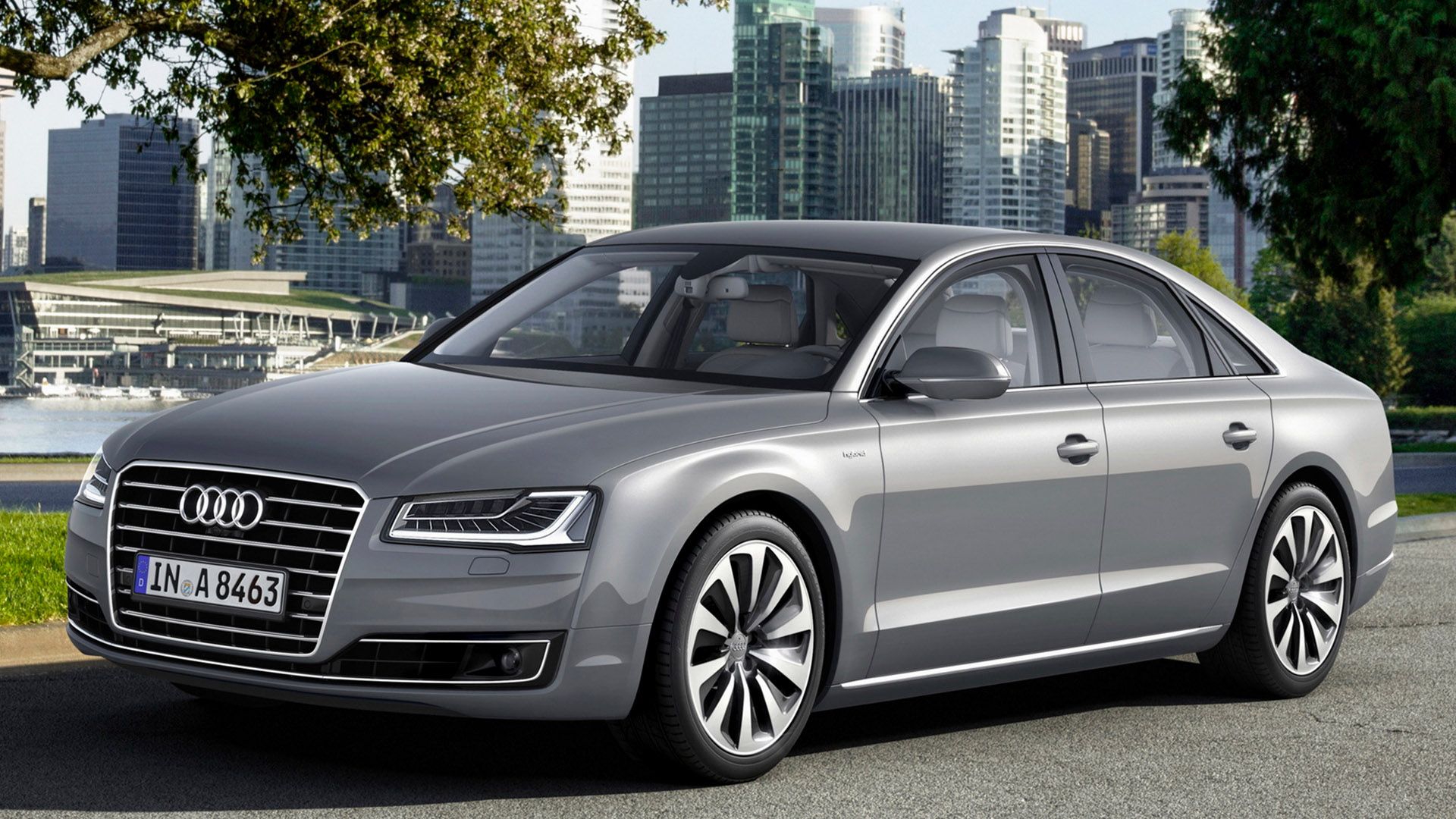 Matt grey Audi A8 hybrid driving on a road, in the background you can see water and a skyline with skyscrapers