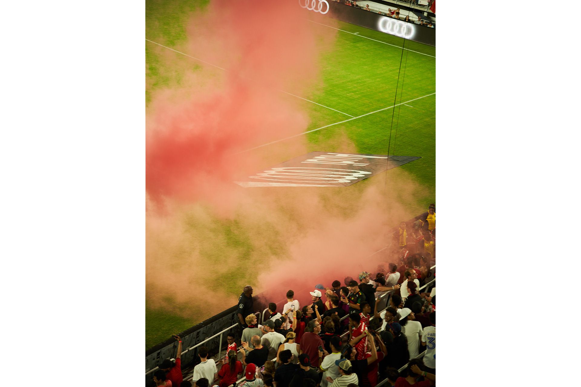 Fans auf der Tribüne in einer roten Pyro-Wolke