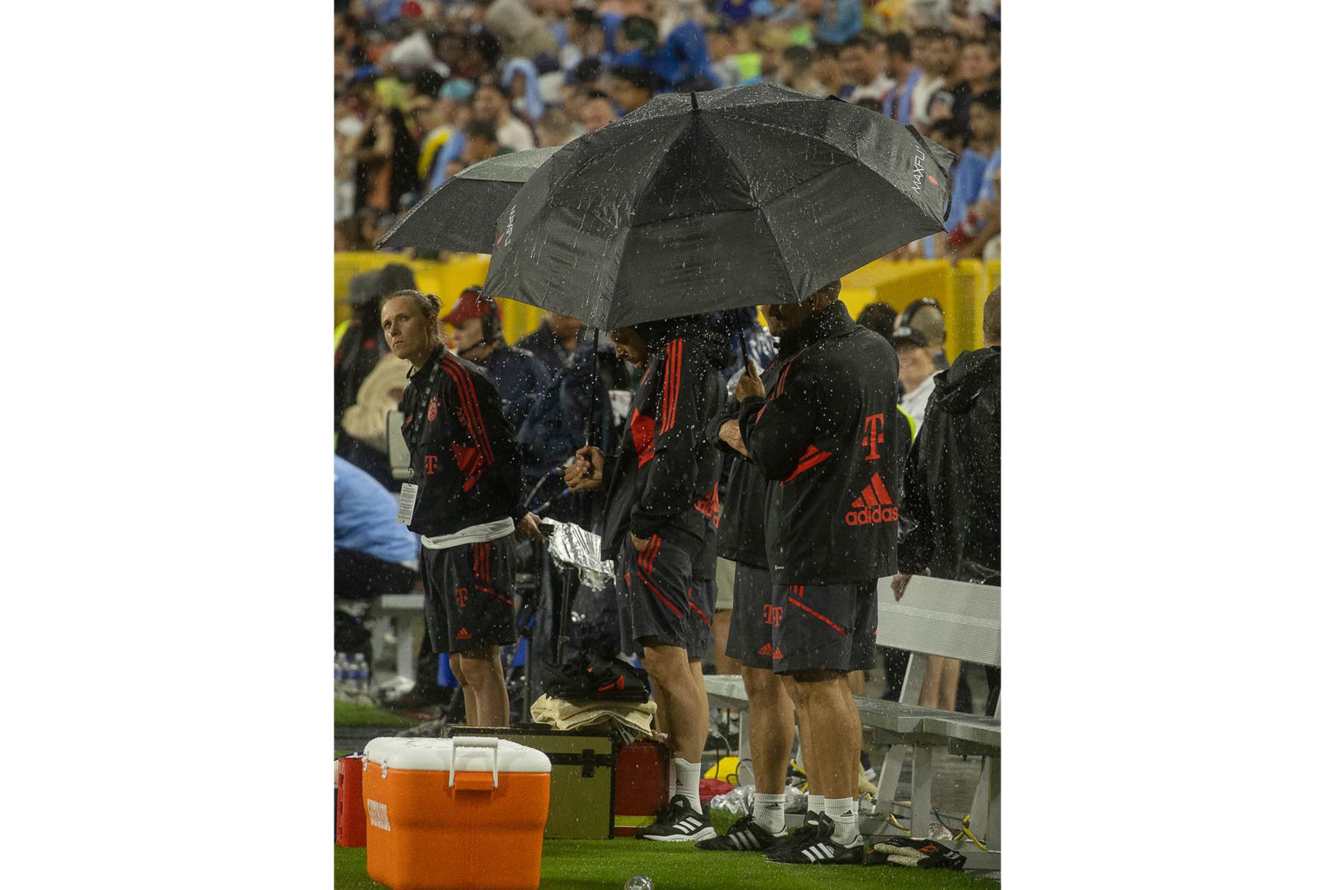 Das Team an der Seitenlinie unter großen, schwarzen Regenschirmen