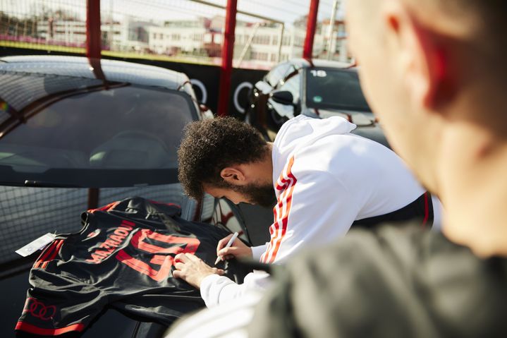 Spieler signiert Trikot auf der Motorhaube seines neuen Audi
