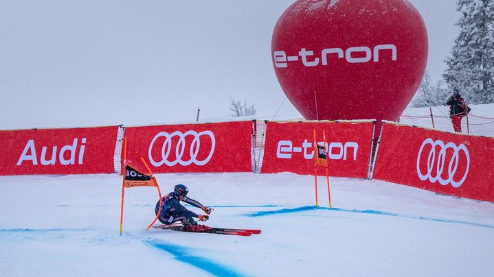 A skier in the bend. In the background, red bands with the Audi logo and the lettering e-tron as well as a red balloon with the lettering e-tron.