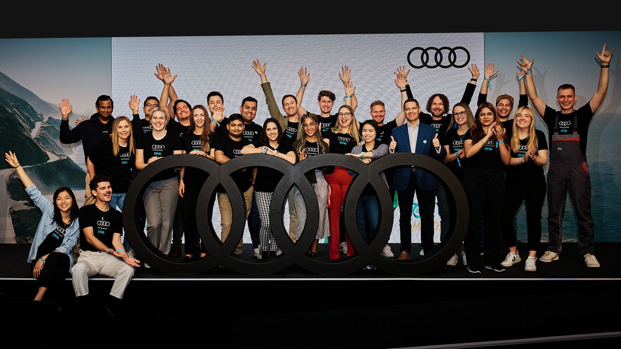 Crowd stands in front of screen with Audi logo and cheer